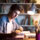 young man student studying at home office desk writing computer lamp